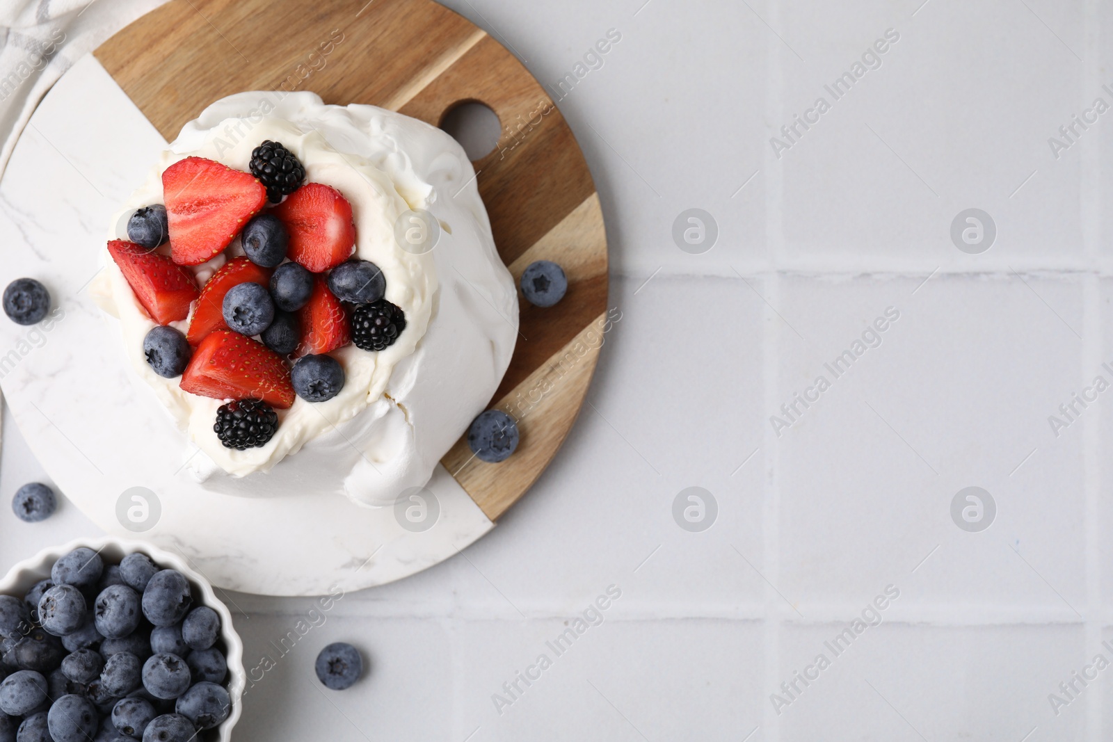 Photo of Pavlova cake (meringue dessert) with whipped cream and fresh berries on white tiled table, top view. Space for text