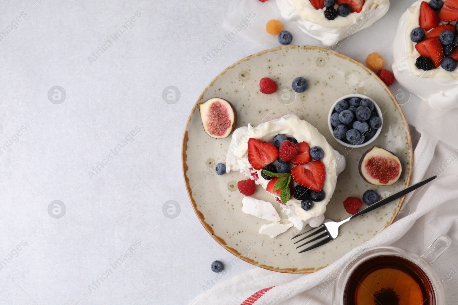 Photo of Pavlova cake (meringue dessert) with whipped cream, fresh berries, mint and fig on light table, top view. Space for text