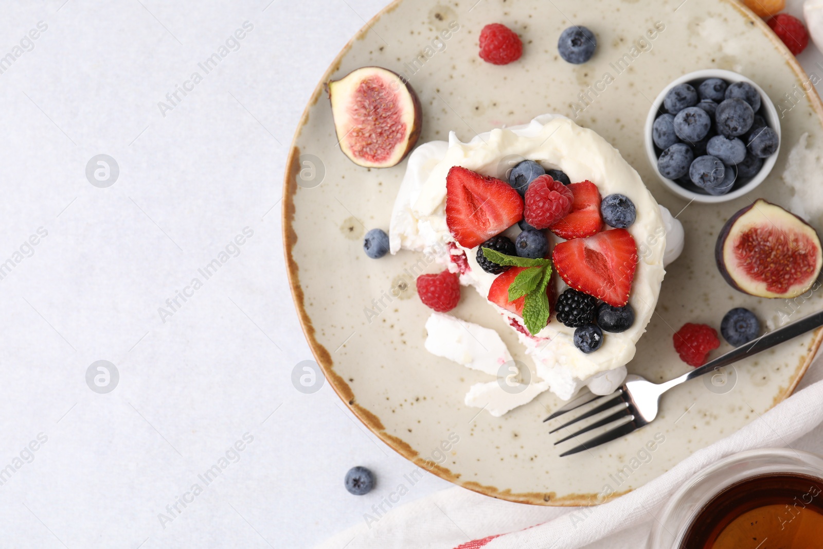 Photo of Pavlova cake (meringue dessert) with whipped cream, fresh berries, mint and fig on light table, top view. Space for text