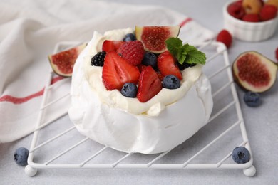 Photo of Pavlova cake (meringue dessert) with whipped cream, fresh berries, mint and fig on light grey table, closeup