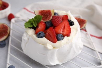 Photo of Pavlova cake (meringue dessert) with whipped cream, fresh berries, mint and fig on light grey table, closeup