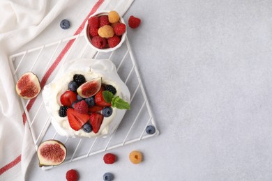 Photo of Pavlova cake (meringue dessert) with whipped cream, fresh berries and fig on light grey table, flat lay. Space for text