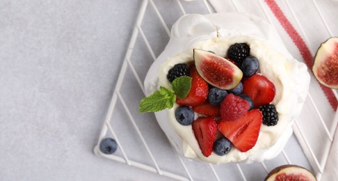 Photo of Pavlova cake (meringue dessert) with whipped cream, fresh berries, mint and fig on light grey table, top view