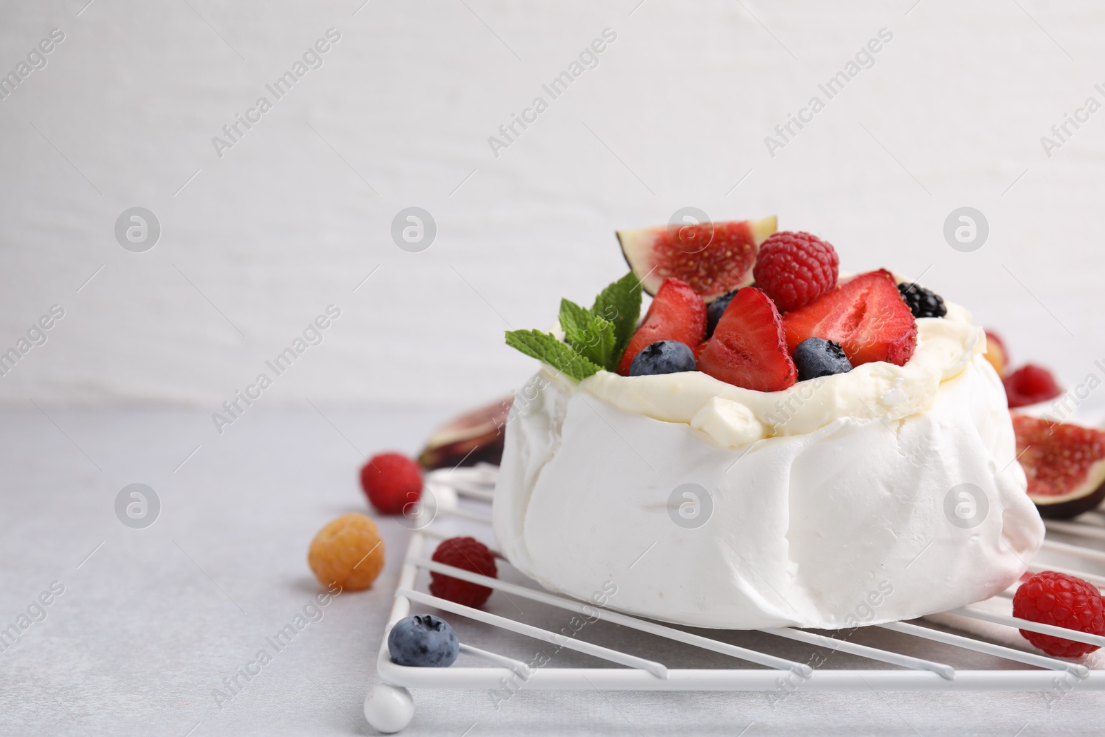 Photo of Pavlova cake (meringue dessert) with whipped cream, fresh berries, mint and fig on light grey table, closeup