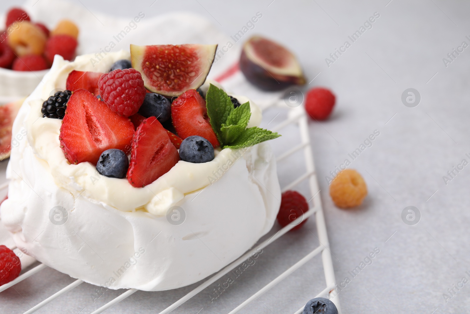 Photo of Pavlova cake (meringue dessert) with whipped cream, fresh berries, mint and fig on light grey table, closeup