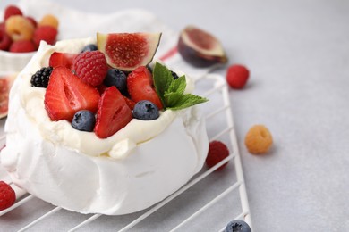 Photo of Pavlova cake (meringue dessert) with whipped cream, fresh berries, mint and fig on light grey table, closeup