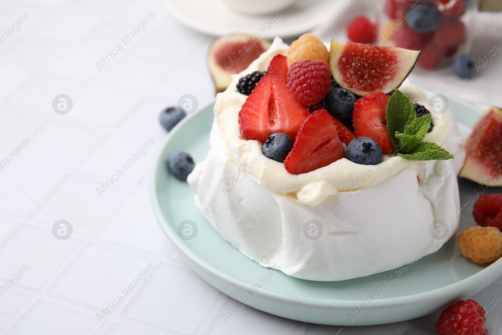 Photo of Pavlova cake (meringue dessert) with whipped cream, fresh berries, mint and fig on white tiled table, closeup