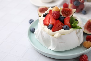 Photo of Pavlova cake (meringue dessert) with whipped cream, fresh berries, mint and fig on white tiled table, closeup