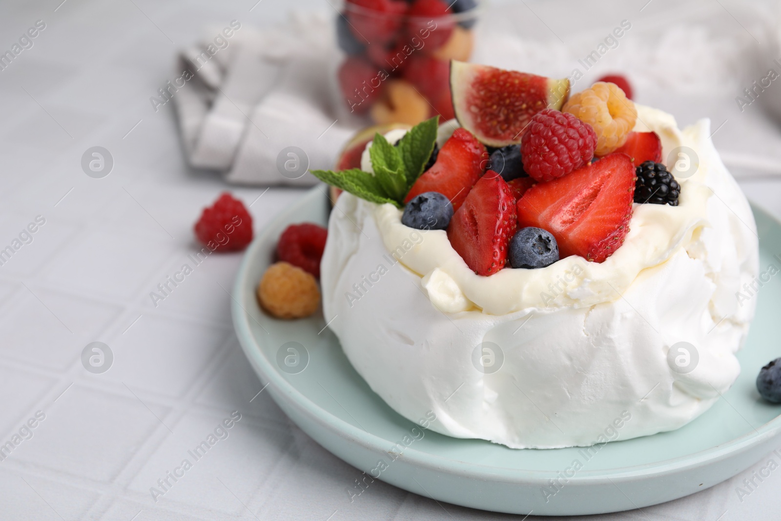 Photo of Pavlova cake (meringue dessert) with whipped cream, fresh berries, mint and fig on white tiled table, closeup