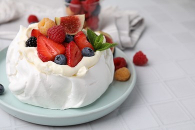 Photo of Pavlova cake (meringue dessert) with whipped cream, fresh berries, mint and fig on white tiled table, closeup