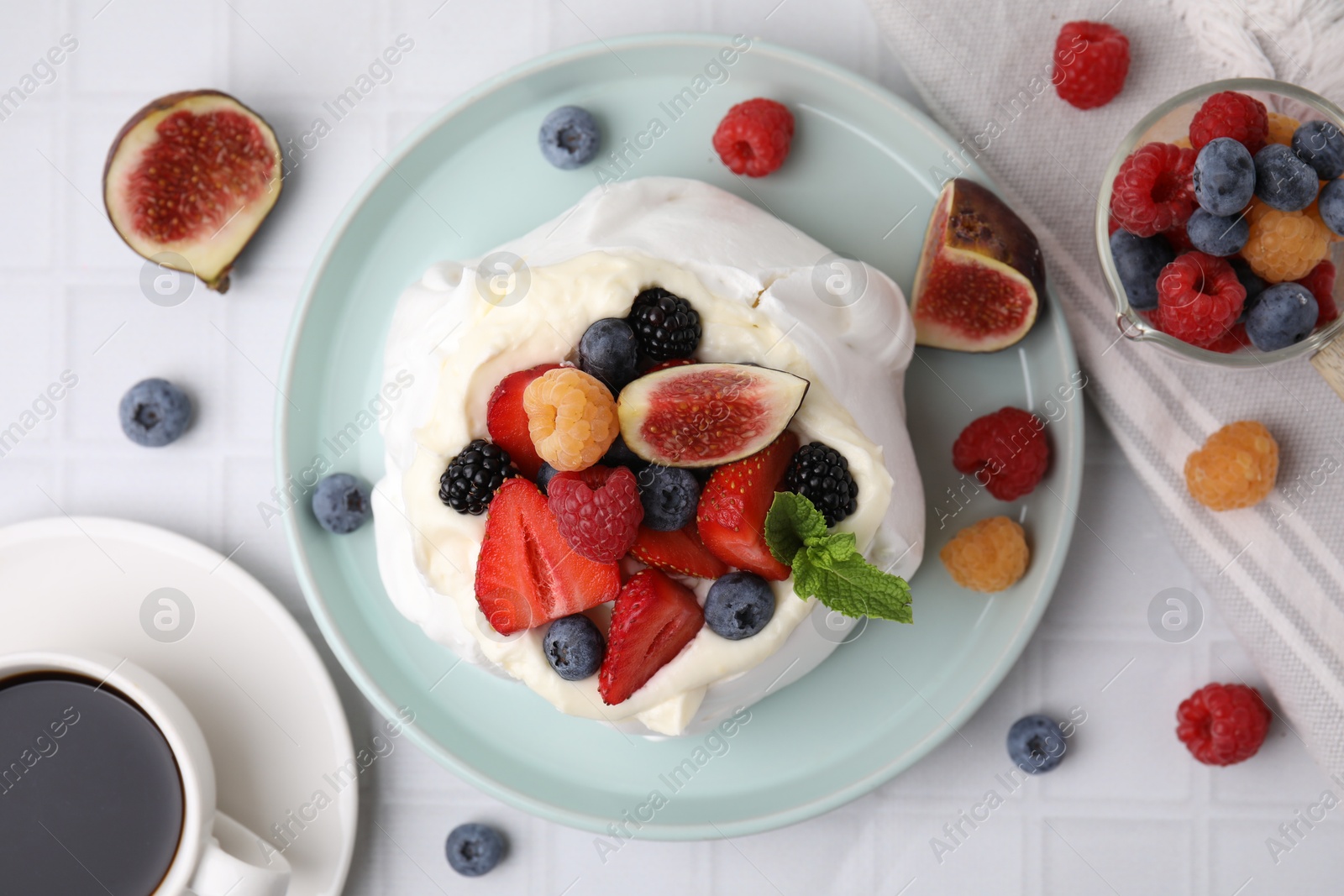 Photo of Pavlova cake (meringue dessert) with whipped cream, fresh berries, mint and fig on white tiled table, flat lay