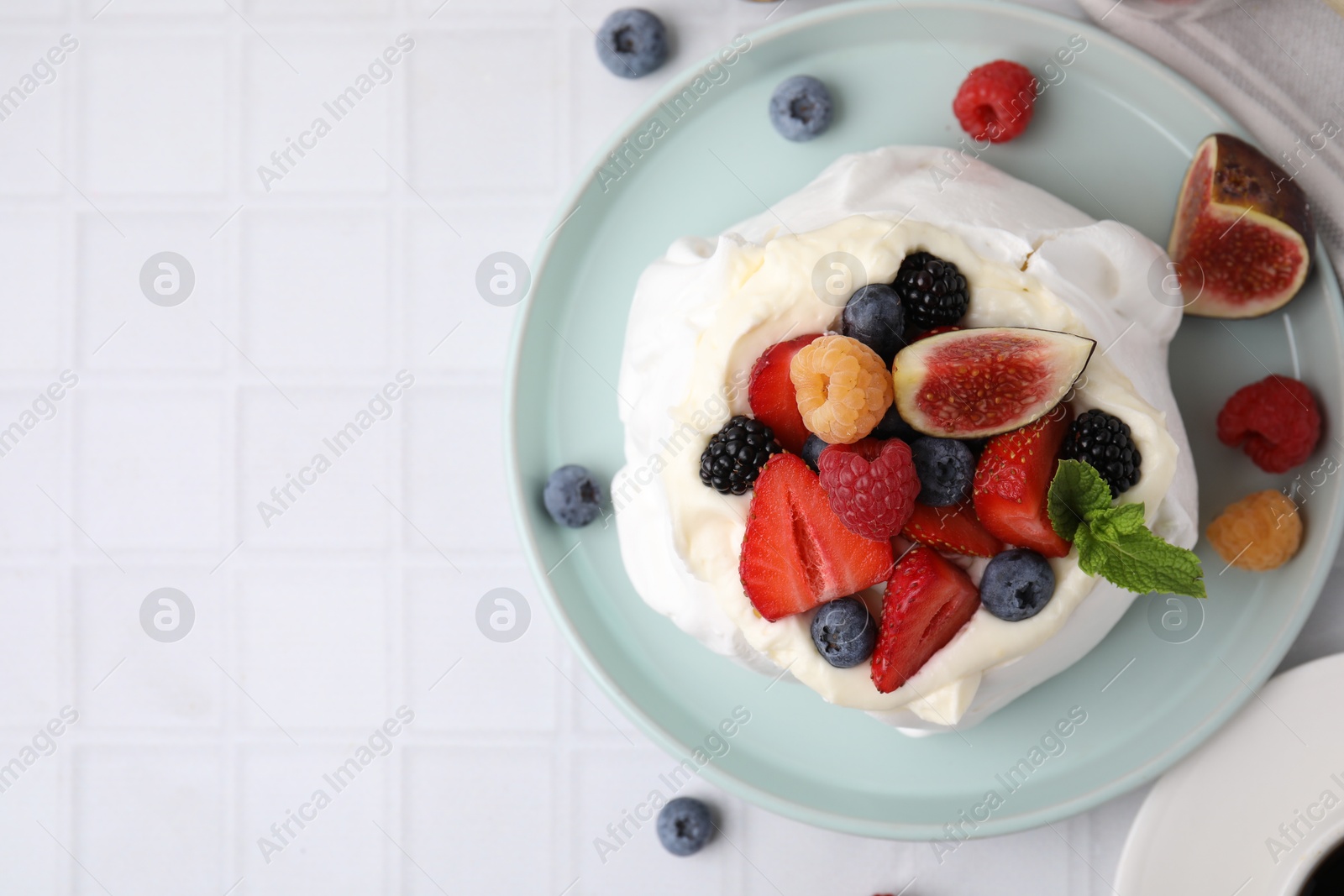 Photo of Pavlova cake (meringue dessert) with whipped cream, fresh berries, mint and fig on white tiled table, top view. Space for text