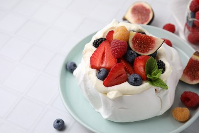 Photo of Pavlova cake (meringue dessert) with whipped cream, fresh berries, mint and fig on white tiled table, closeup