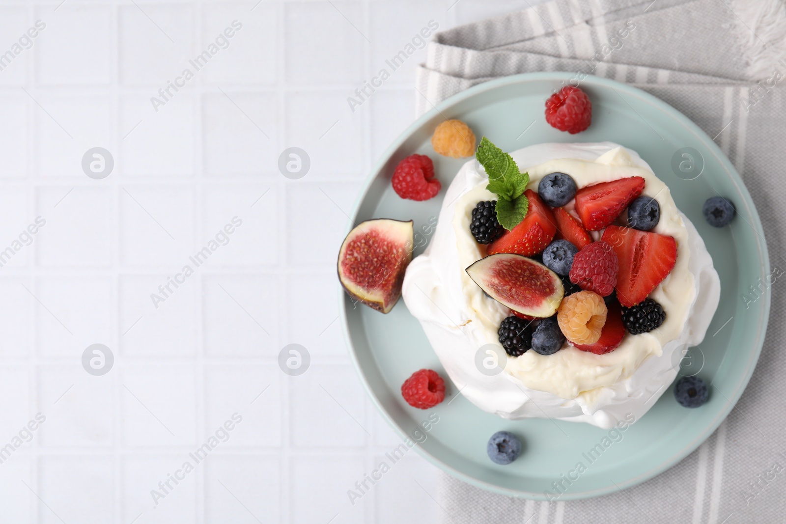 Photo of Pavlova cake (meringue dessert) with whipped cream, fresh berries, mint and fig on white tiled table, top view. Space for text