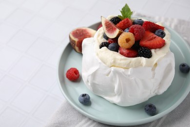 Photo of Pavlova cake (meringue dessert) with whipped cream, fresh berries, mint and fig on white tiled table, closeup