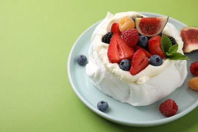 Photo of Pavlova cake (meringue dessert) with whipped cream, fresh berries, mint and fig on green background, closeup