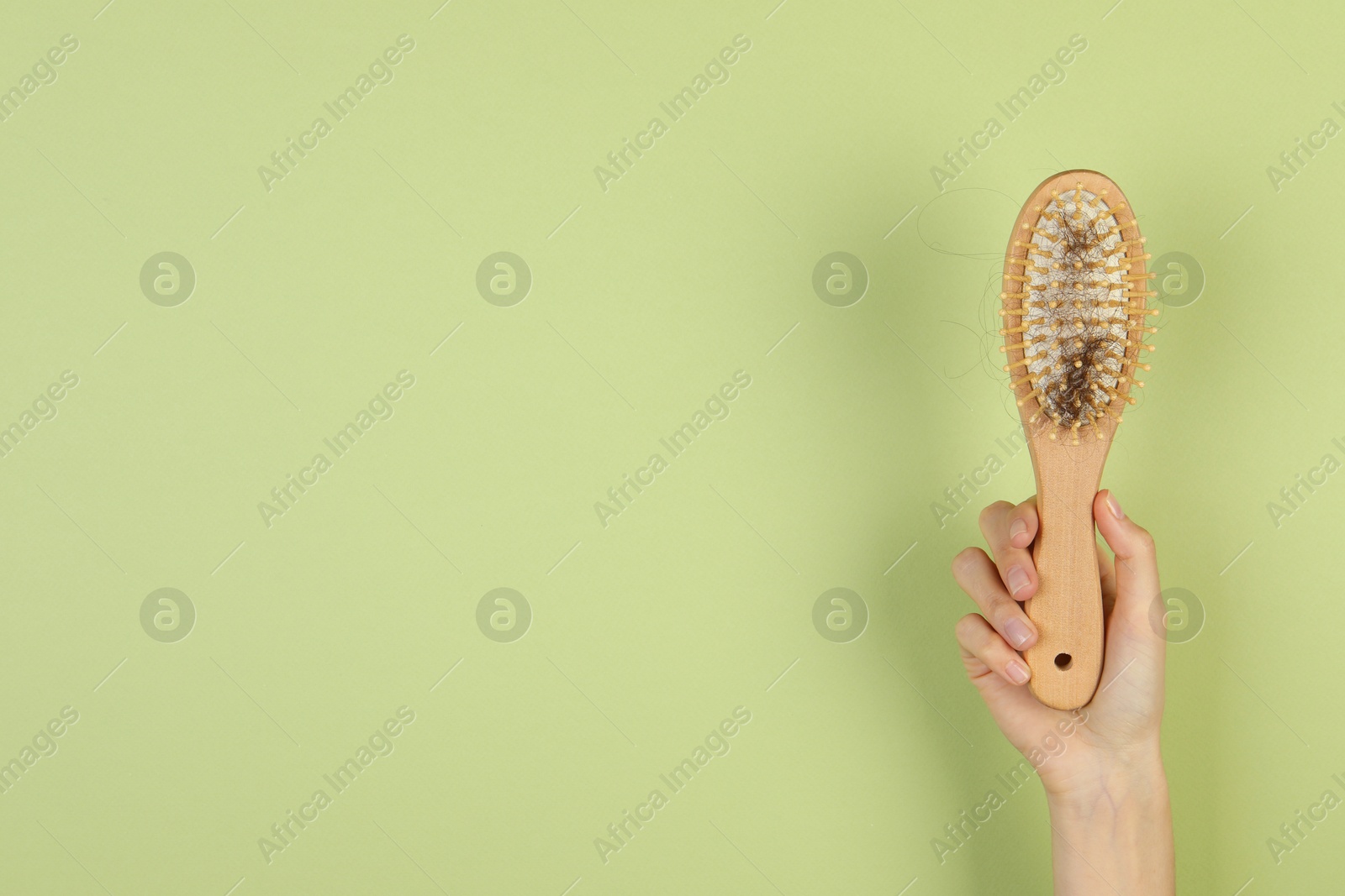 Photo of Woman holding brush with lost hair on olive background, closeup. Space for text