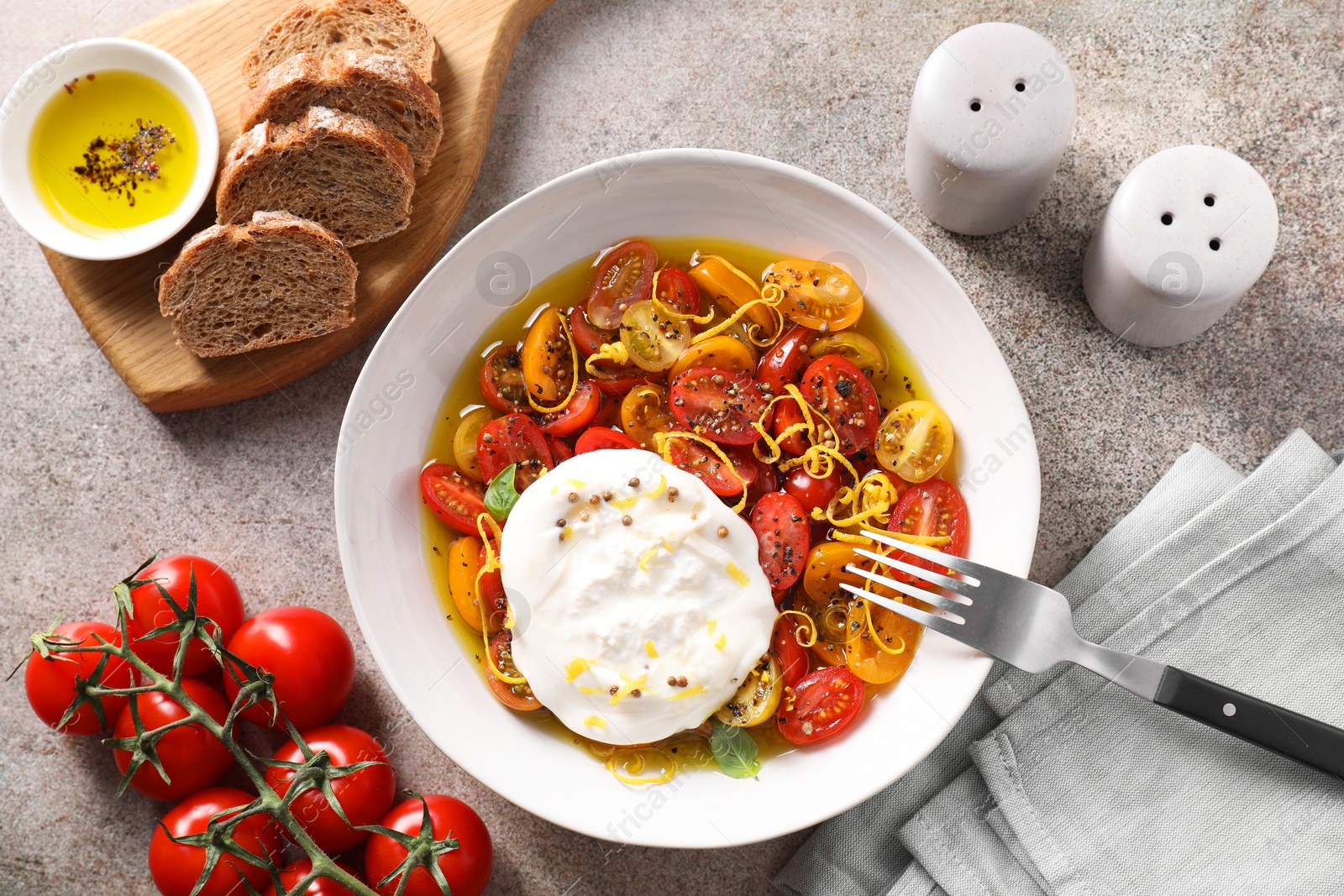 Photo of Delicious fresh burrata salad in bowl served on gray textured table, flat lay