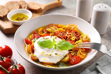 Photo of Delicious fresh burrata salad in bowl served on gray textured table, closeup