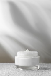 Photo of Face cream in jar on grey textured table. Cosmetic product