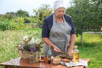 Photo of Senior woman making tincture at wooden table outdoors