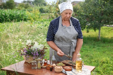 Photo of Senior woman making tincture at wooden table outdoors