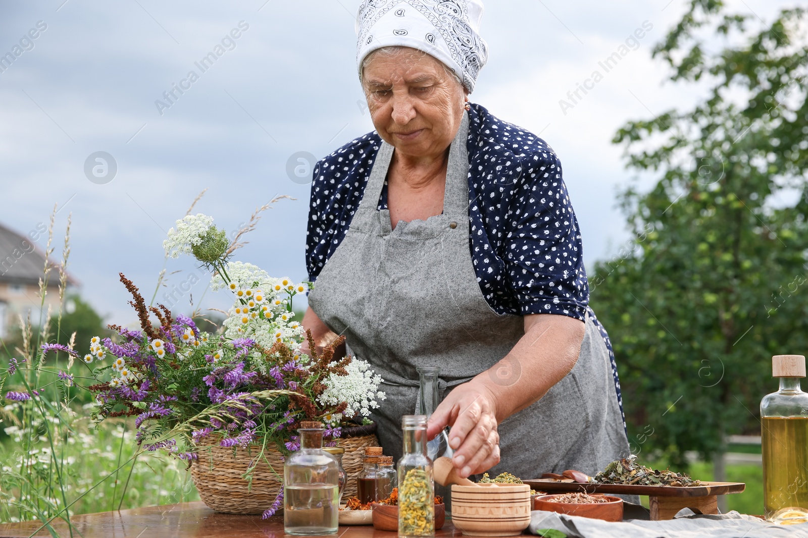 Photo of Senior woman making tincture at table outdoors