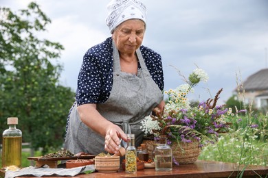 Photo of Senior woman making tincture at table outdoors