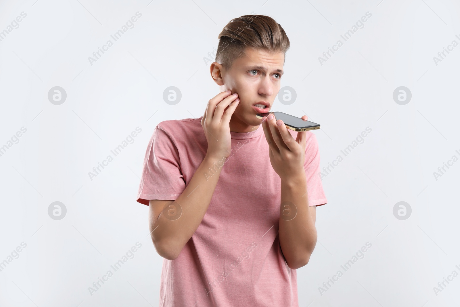 Photo of Young man recording voice message via smartphone on light gray background