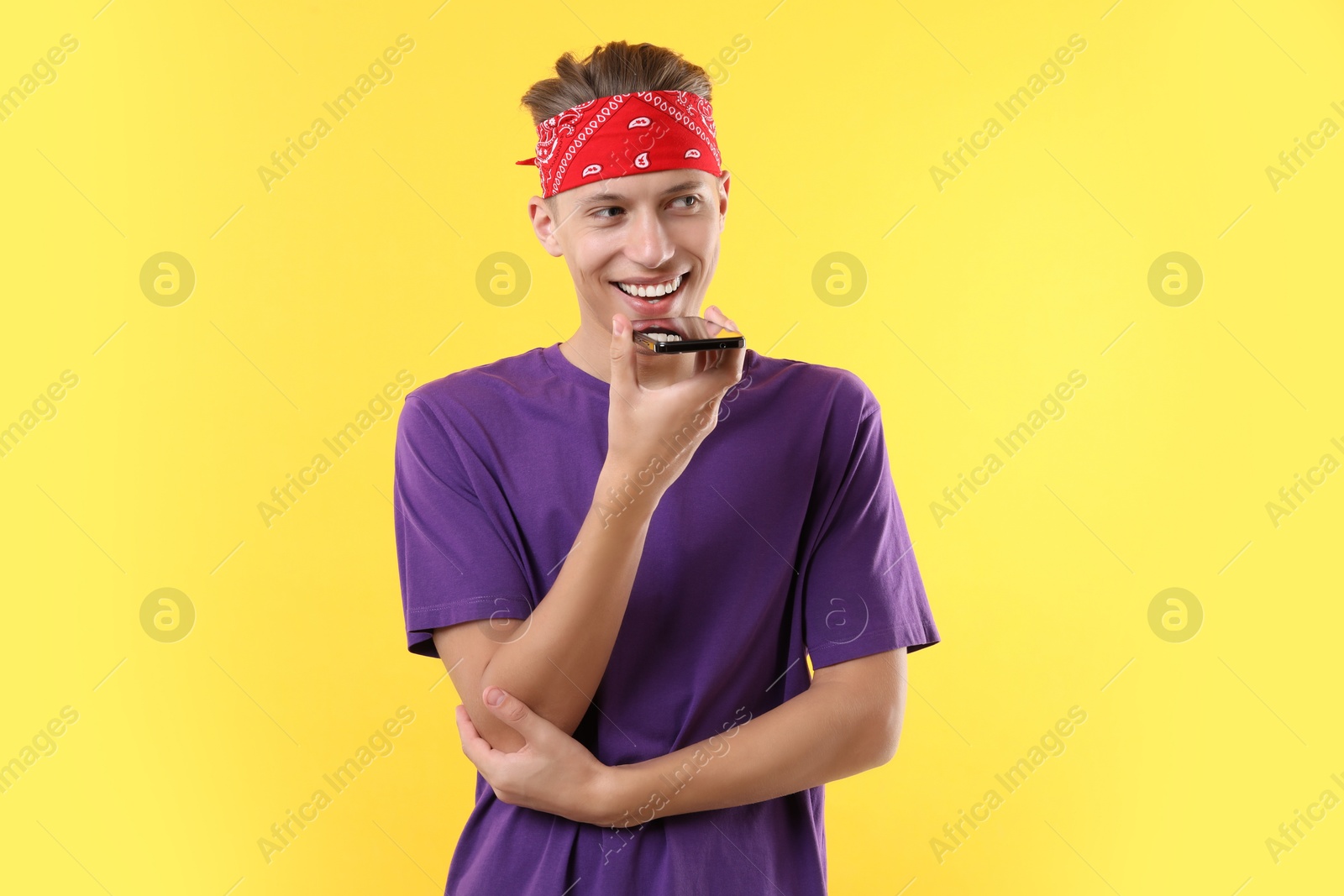 Photo of Young man recording voice message via smartphone on yellow background