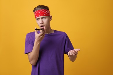 Young man recording voice message via smartphone on orange background