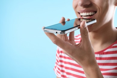 Young man recording voice message via smartphone on light blue background, closeup. Space for text