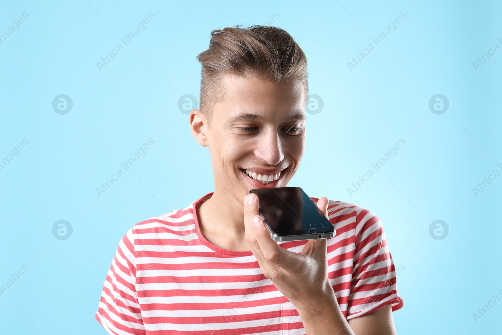 Photo of Young man recording voice message via smartphone on light blue background