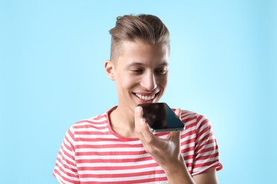 Young man recording voice message via smartphone on light blue background