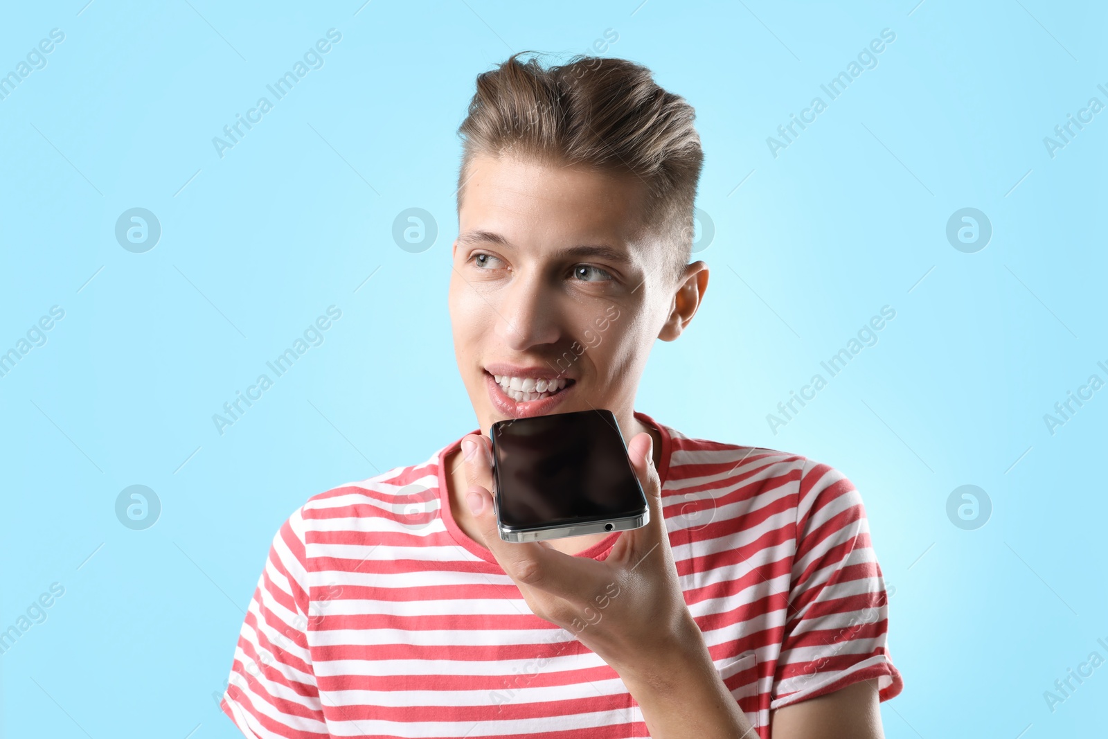 Photo of Young man recording voice message via smartphone on light blue background