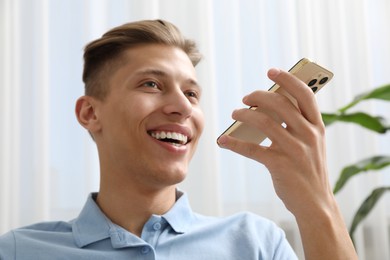 Young man recording voice message via smartphone at home, selective focus