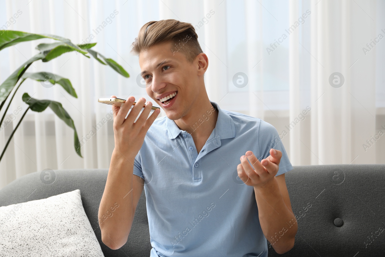 Photo of Young man recording voice message via smartphone at home