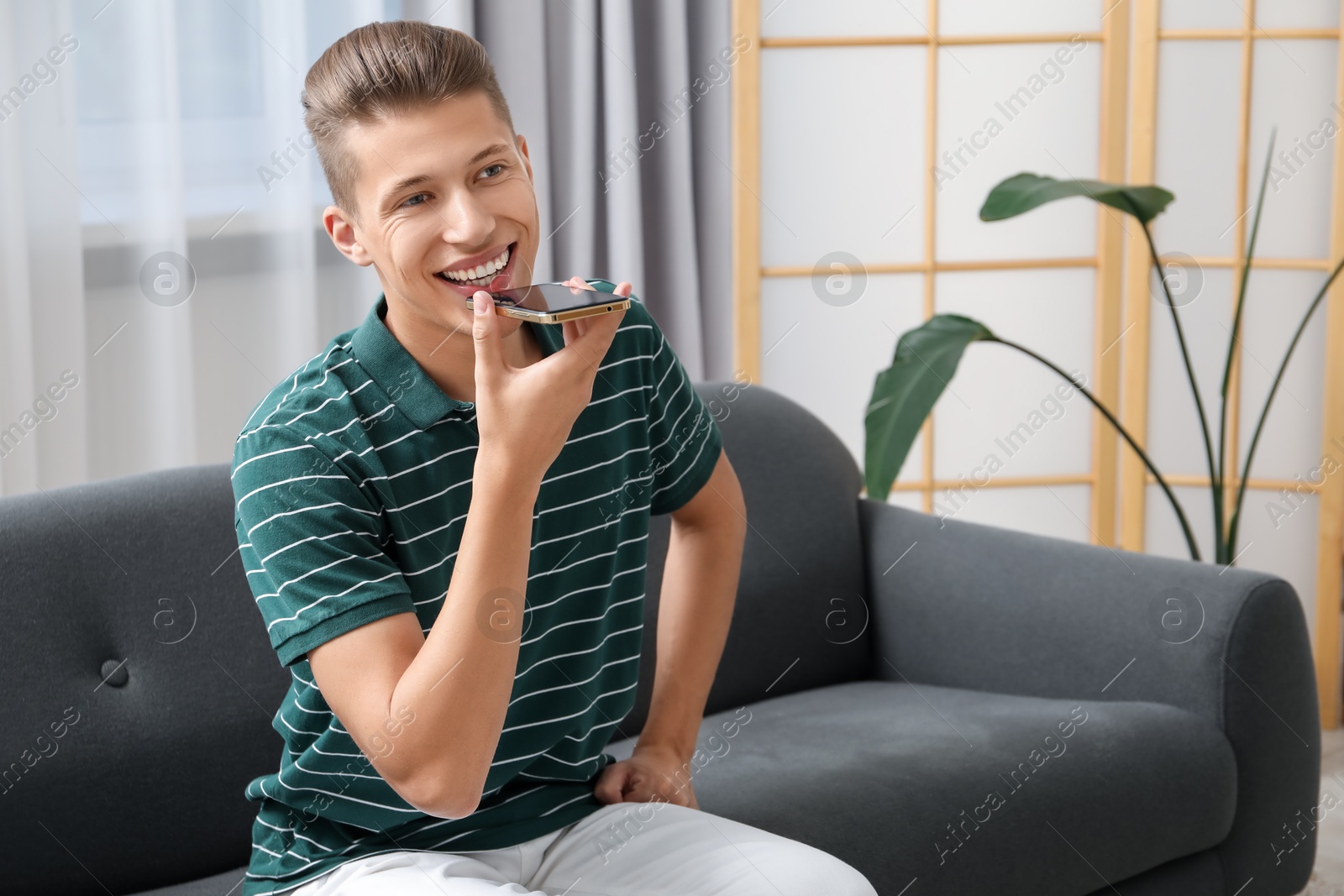 Photo of Young man recording voice message via smartphone at home