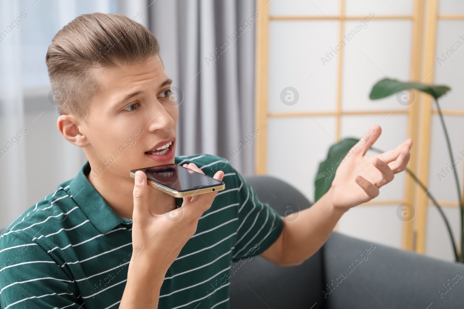 Photo of Young man recording voice message via smartphone at home