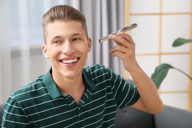 Photo of Young man with smartphone listening to voice message at home