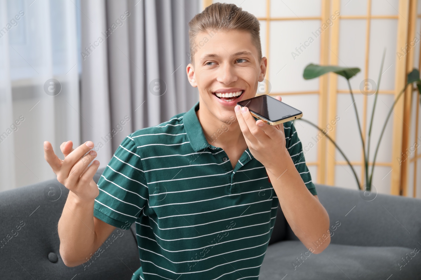 Photo of Young man recording voice message via smartphone at home