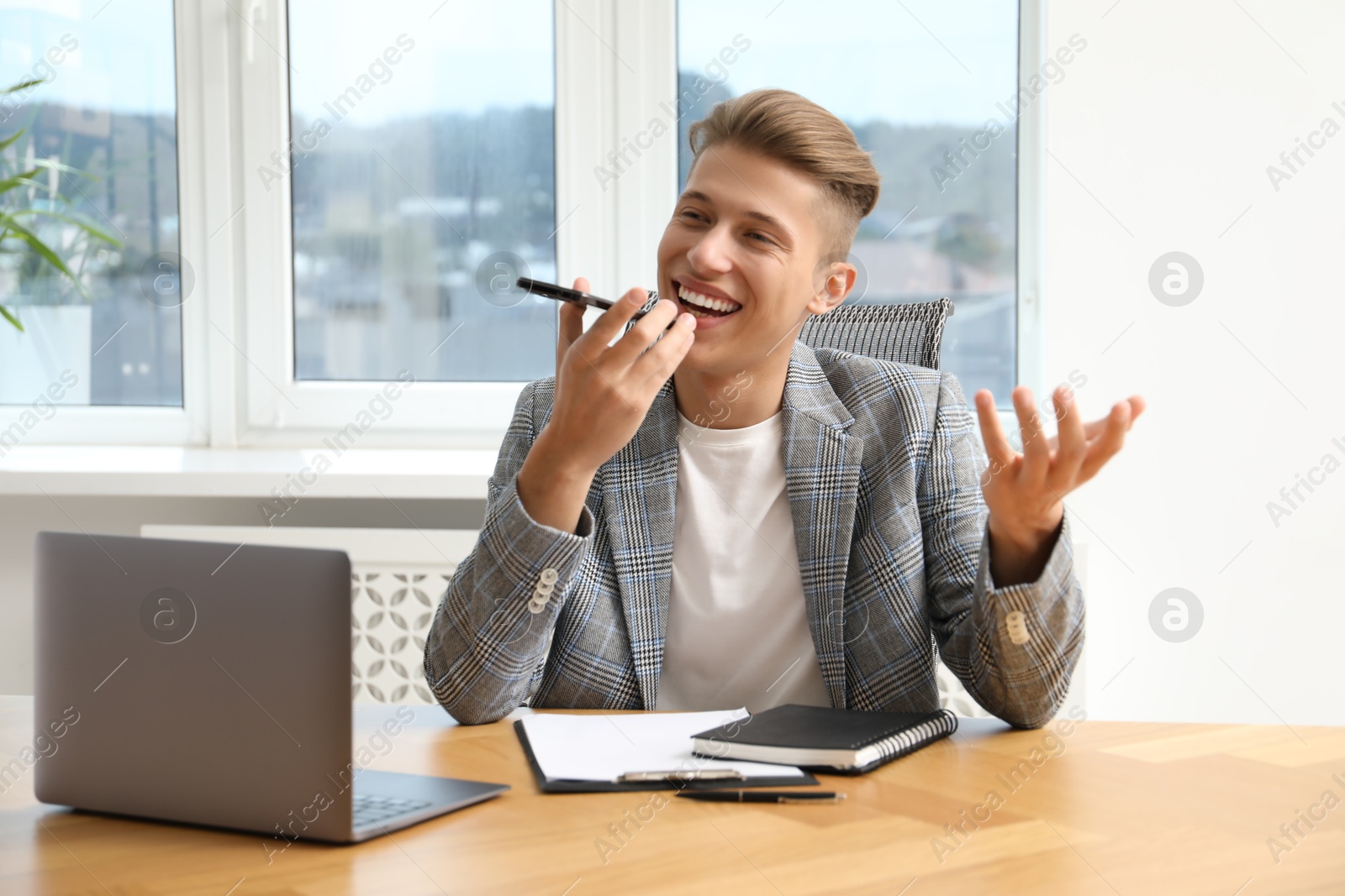 Photo of Young man recording voice message via smartphone in office