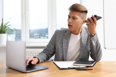 Photo of Young man with smartphone listening to voice message in office