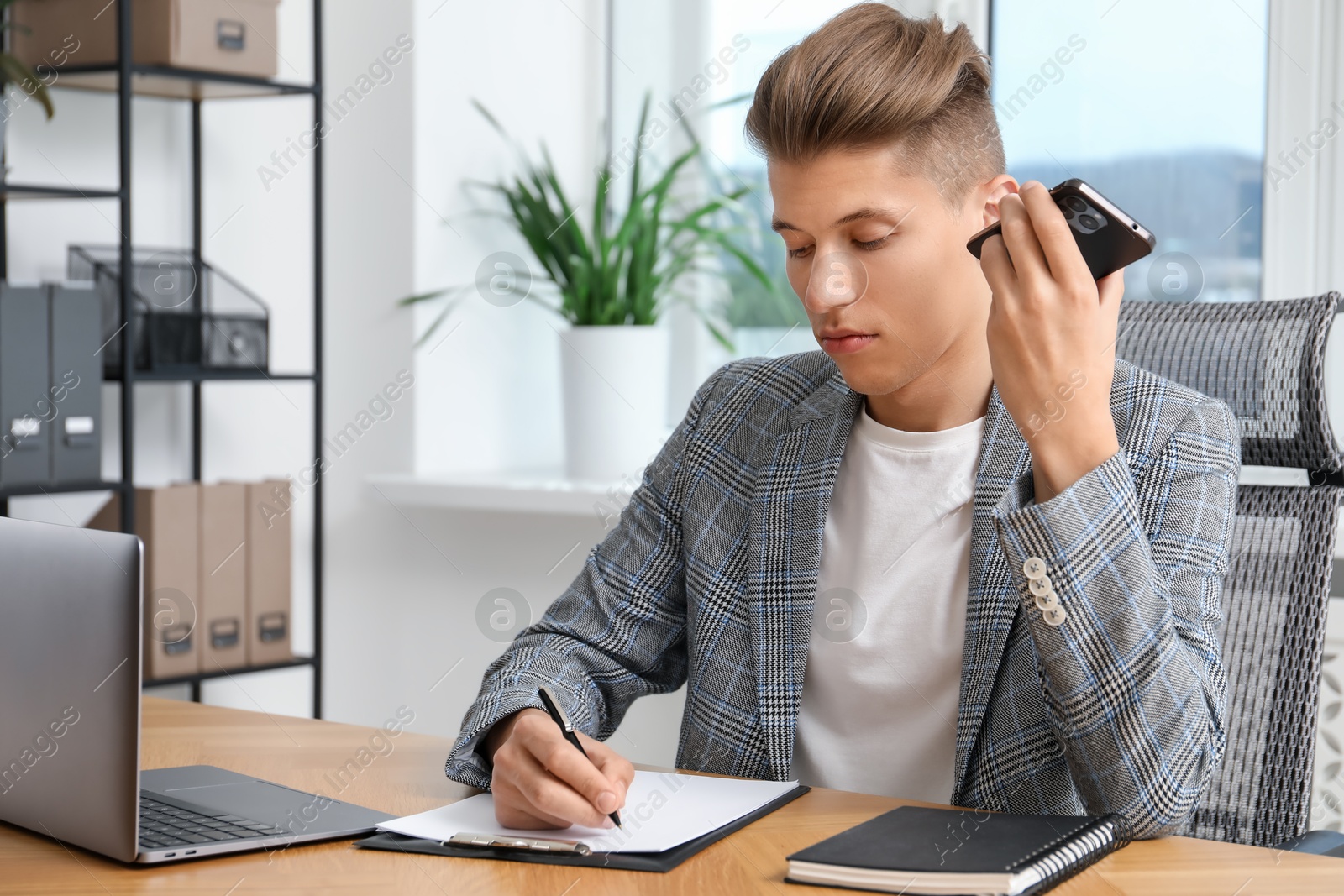 Photo of Young man with smartphone listening to voice message in office