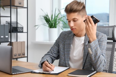 Photo of Young man with smartphone listening to voice message in office