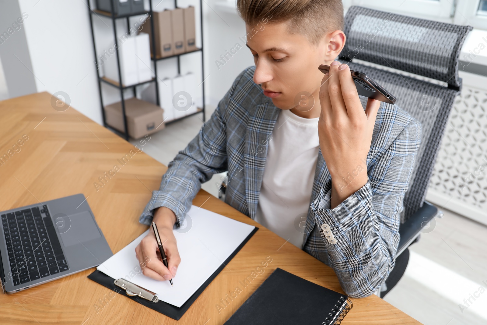 Photo of Young man with smartphone listening to voice message in office