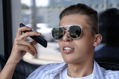 Young man with smartphone listening to voice message in outdoor cafe