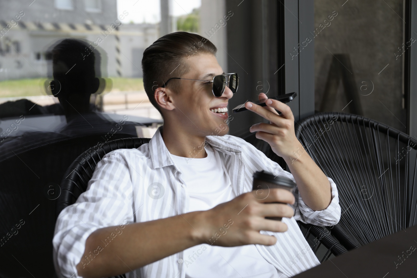 Photo of Young man recording voice message via smartphone in outdoor cafe