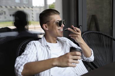 Young man recording voice message via smartphone in outdoor cafe