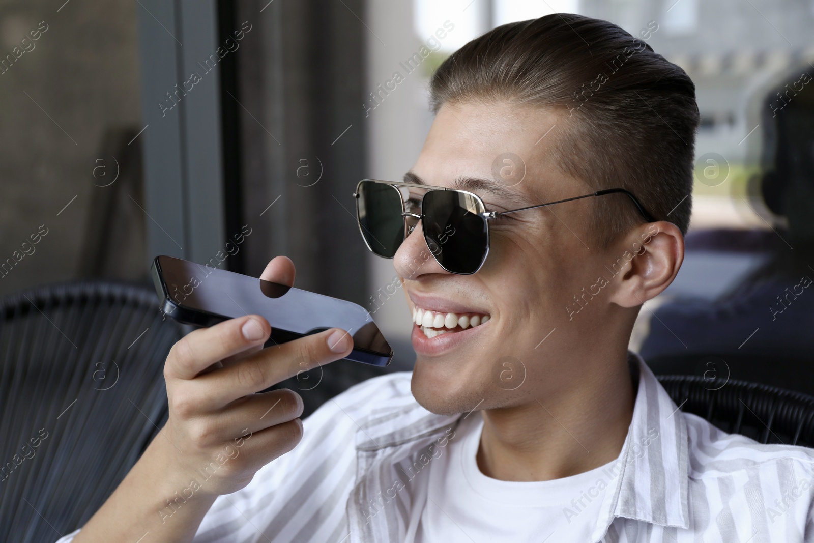 Photo of Young man recording voice message via smartphone in outdoor cafe